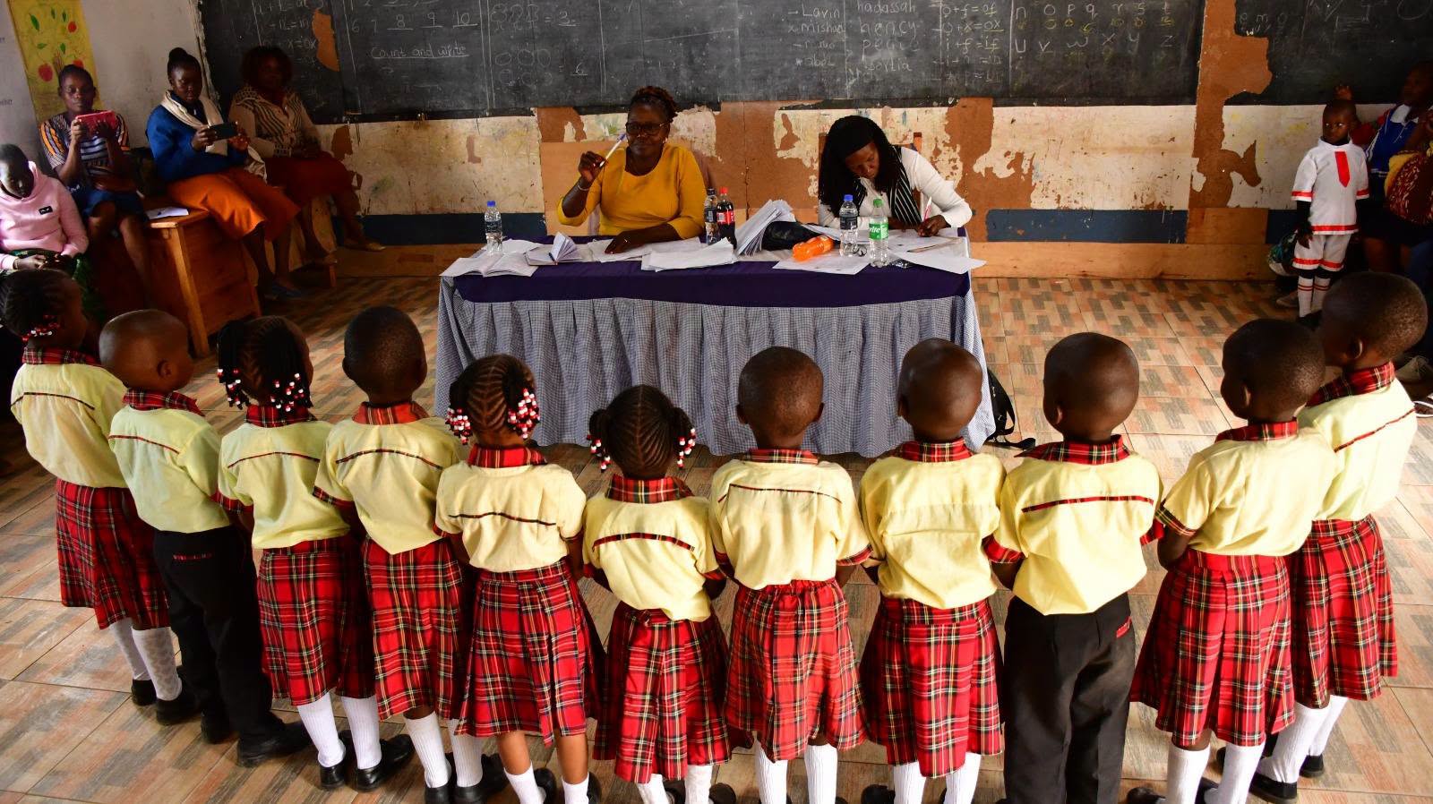 Early years learners in red and yellow uniforms line up in a classroom
