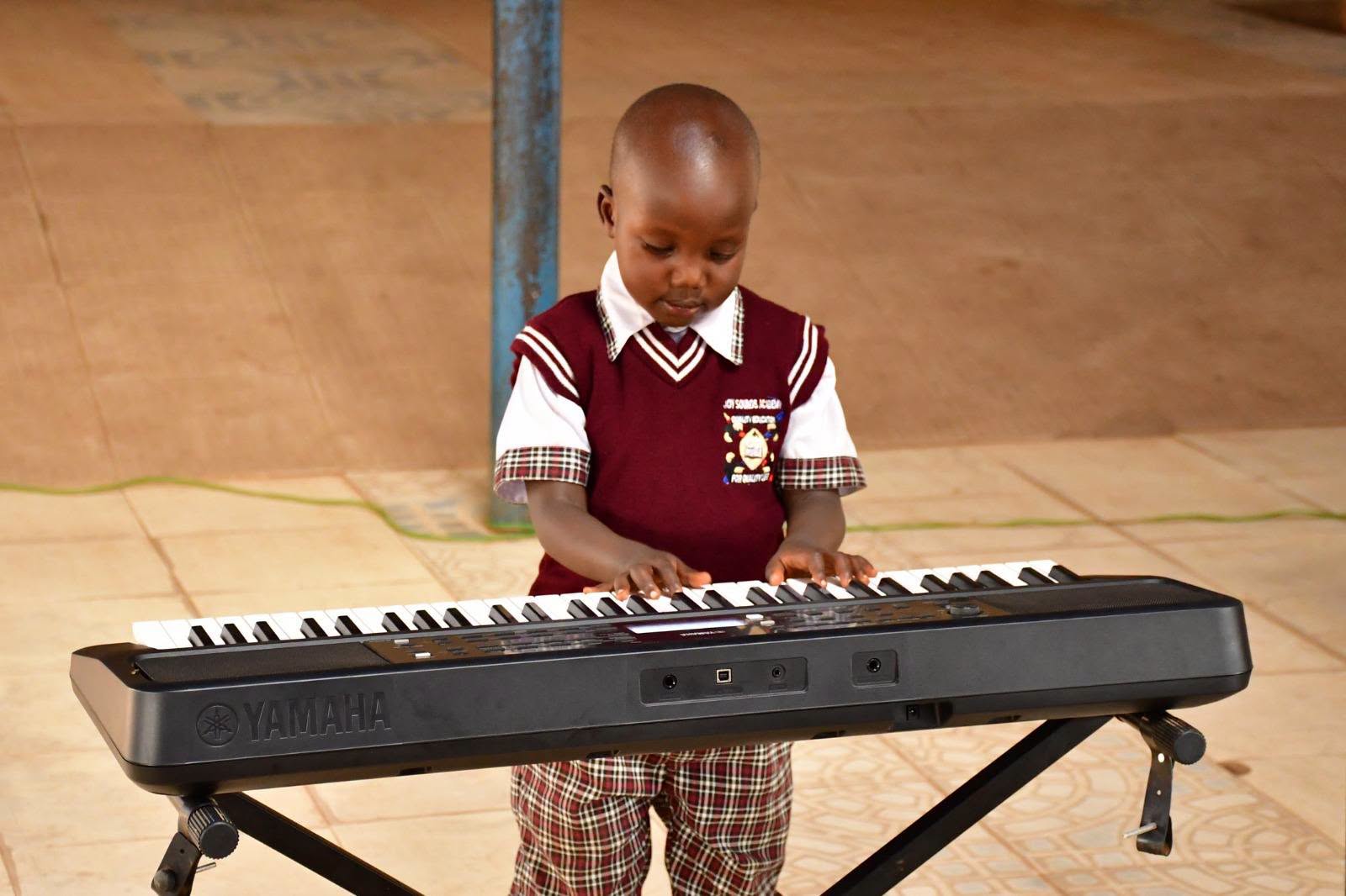 A young learner in a maroon school sweater plays an electronic keyboard